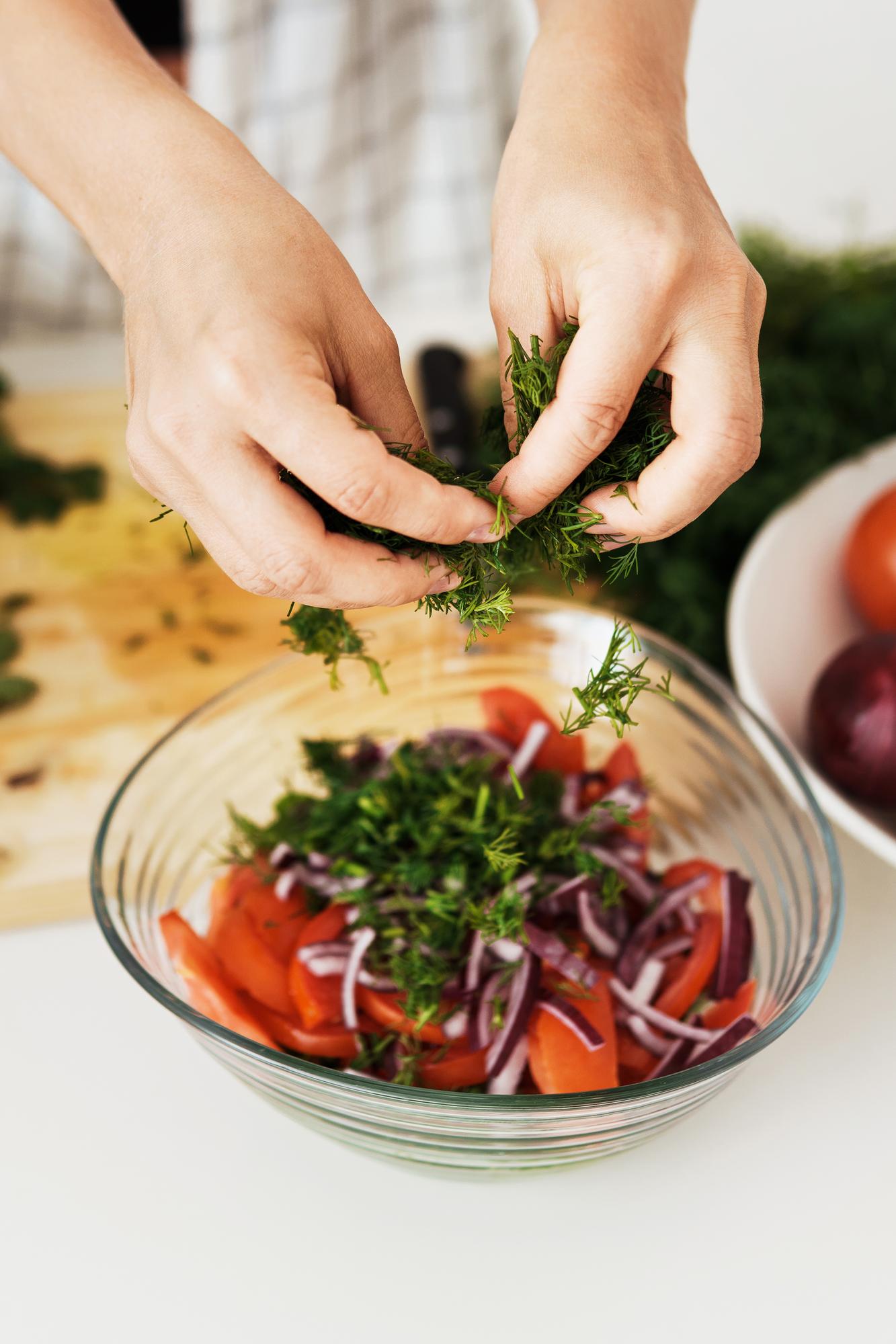 hands plating a vibrant bowl with herbs